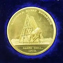 A gold medal, featuring an image of a telescope. Engraved with 'Asaph Hall 1979' and 'quicquid nitet notandum'