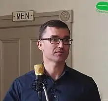 Man with glasses speaking at a microphone