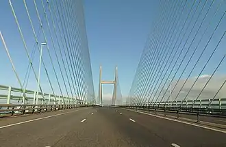 A three-lane motorway goes into the distance, flanked by blueish cables which hold up the Prince of Wales Bridge